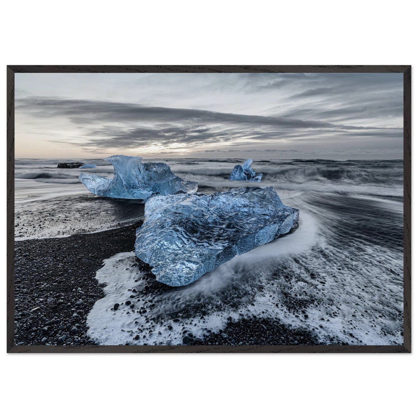 Landscape photography showcases the delicate harmony between blue ice and water, seamlessly intertwined with the dramatic black stones on the beach. Poster. Frame.