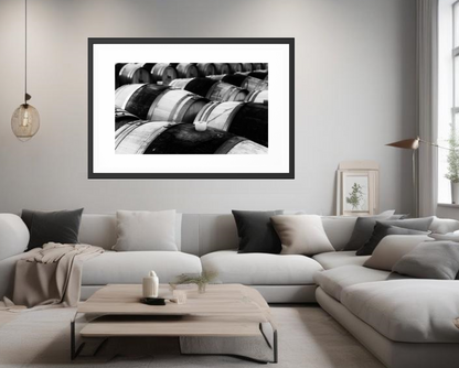 Framed black and white abstract art above a modern living room sofa. Row of wooden barrels with a white cap in the foreground. A stylish photography in black and white ideal for minimalistic modern or rustic spaces, an even for bohemian ones.