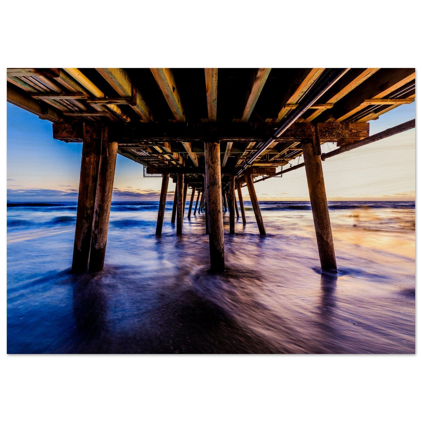 A photographic print depicting the underside of a wooden pier extending into calm waters, with a blend of light gold, blue, and purple colors representing a harmonious palette of nature and human craftsmanship.