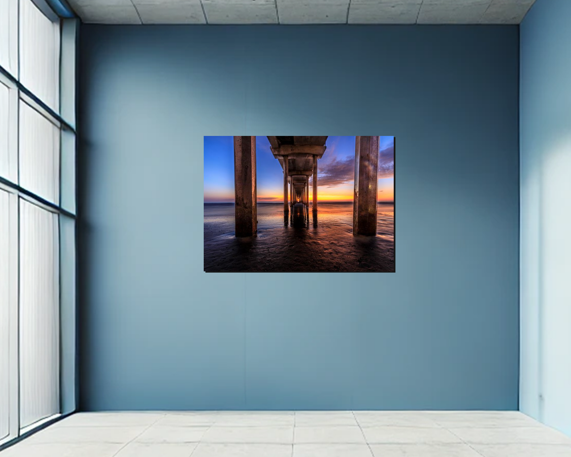 Wall art of a sunset under a pier in a room with large windows.