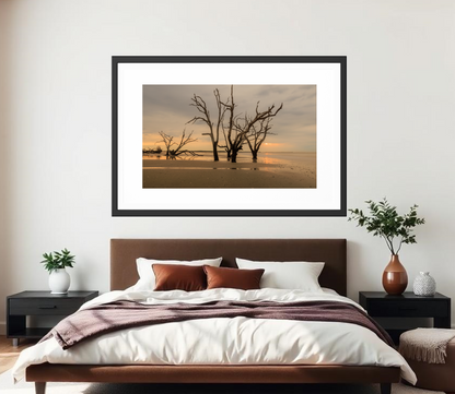 Framed artwork of trees on a beach above a bed in a bedroom. 