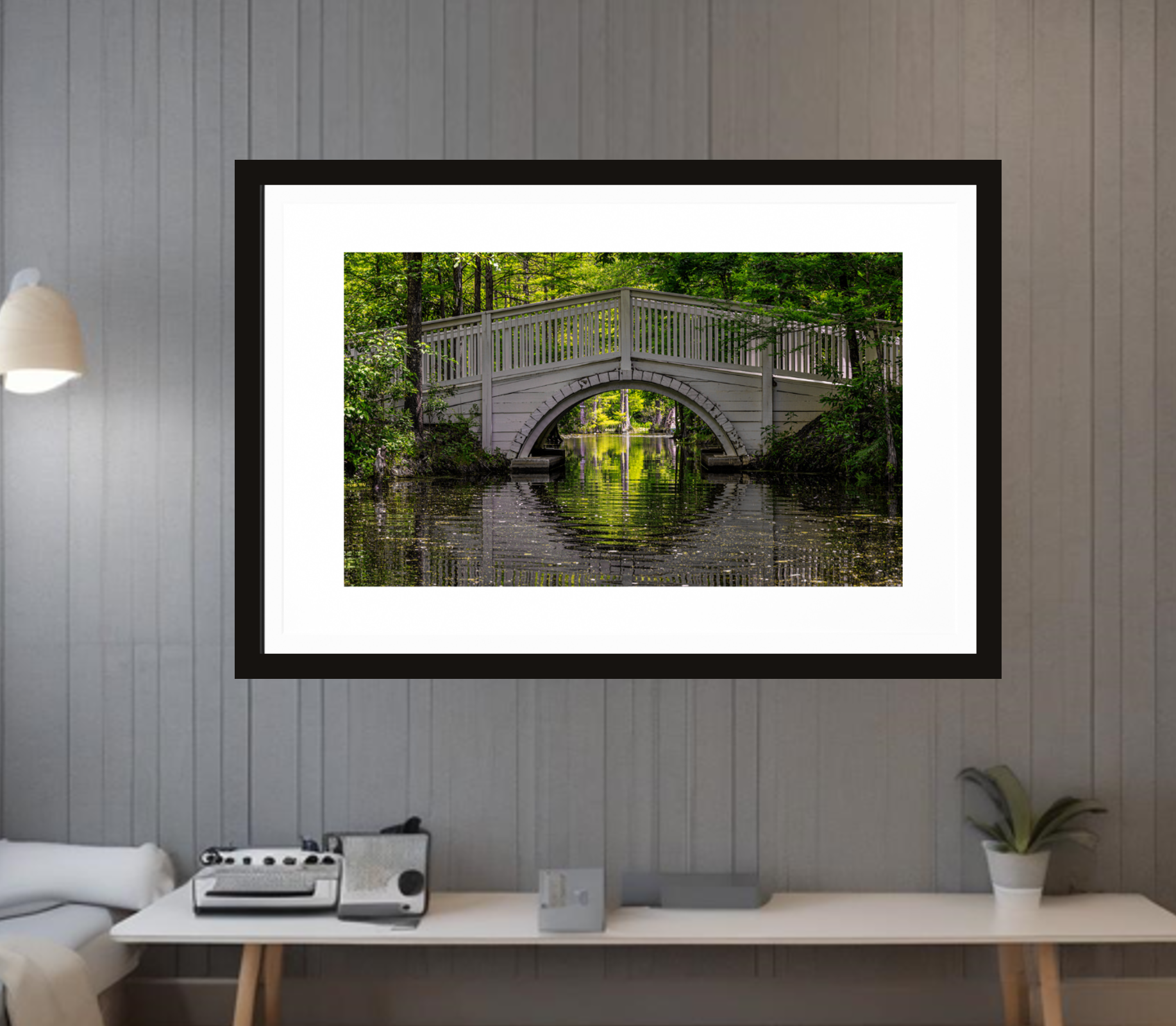 Framed photograph of a bridge over water in a forest, displayed on a wall above a desk elevating the space with decoration with soul.